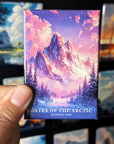 A hand holding a magnet with a colorful illustration of a mountain landscape, with the text "GATES OF THE ARCTIC NATIONAL PARK" printed on it.