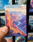 A hand holding a magnet with a colorful illustration of the Grand Canyon.