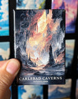 A hand holding a magnet with an illustration of a cave scene, with the text "CARLSBAD CAVENS NATIONAL PARK" printed on it.