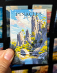 A hand holding a magnet depicting a scenic landscape with mountains, trees, and a river.
