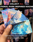 A hand holding a collection of four national park-inspired magnets, each depicting a unique landscape.