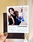 A person is holding a small photo album with a photo of a young girl and a baby, along with a calendar for the month of October.