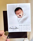 A person is holding a small calendar featuring a photo of a sleeping baby.