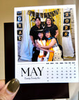 A person is holding a small calendar with a photo of a family posing for a graduation photo.