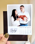 A person is holding a small calendar featuring a photo of a couple with a baby, with the date "July 2026" visible.