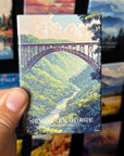 A hand holding a magnet with an illustration of a bridge over a river, surrounded by lush greenery.