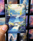 A hand holding a magnet with a painting of a waterfall and forest in the Cuyahoga Valley National Park.