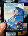 A hand holding a magnet with a scenic image of the Guadalupe Mountains National Park.