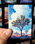 A hand holding a magnet with a picture of a Joshua tree in a desert landscape.