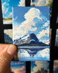 A hand holding a magnet with a picture of a mountain and a lake, with the text "GLACIER BAY NATIONAL PARK" printed on it.