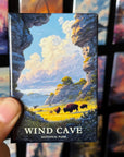 A hand holding a magnet with a landscape scene depicting a wind cave and bison in the background.