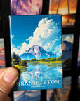 A hand holding a magnet with a scenic image of a mountain and a lake, with the text "GRAND Teton NATIONAL PARK" printed on it.
