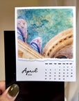 A hand holding a small calendar with a picture of a building and a bird on the cover, and a calendar for the month of April.