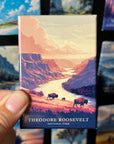 A hand holding a magnet with a scenic landscape of Theodore Roosevelt National Park, featuring a river, mountains, and wildlife.