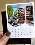 A person's hand holding a small calendar card with a photo of a store interior and shelves filled with various items.