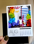 A person is holding a small calendar with a photo of a young girl standing in front of a colorful balloon arch.