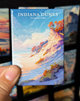 A hand holding a magnet with an illustration of a scenic landscape, specifically the Indiana Dunes National Park.
