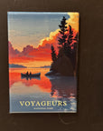 A framed magnet depicting a canoe on a lake with a sunset in the background, surrounded by trees.