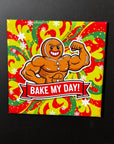 A muscular gingerbread man with a flexed arm, wearing a red and yellow striped shirt, and the text "Bake My Day!" is displayed on a colorful background.