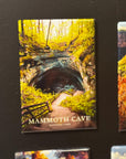The image is a magnet depicting the Mammoth Cave National Park, featuring a scenic view of the cave entrance surrounded by lush vegetation.