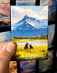 A hand holding a magnet with a picture of a mountain landscape and two bears in the foreground.