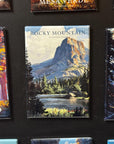a large magnet with a scenic landscape of Rocky Mountain National Park, including a mountain, trees, and a lake.