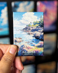 A hand holding a magnet with a scenic image of Acadia National Park, featuring a lighthouse and a rocky coastline with water.