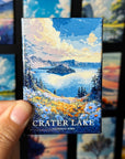 A hand holding a magnet with a painting of Crater Lake in National Park.