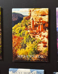 The image is a magnet depicting a scenic landscape with a large rock formation, trees, and mountains.