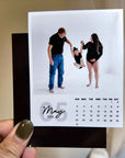 A person holding a small calendar with a photo of a family, including a man, a woman, and a child, posing together.