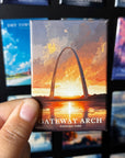 A person's hand holding a magnet with an illustration of the Gateway Arch, a famous monument in Gateway National Park, with a sunset in the background.