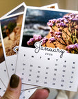 A person's hand holding a small calendar with a photo of a flower on the cover.