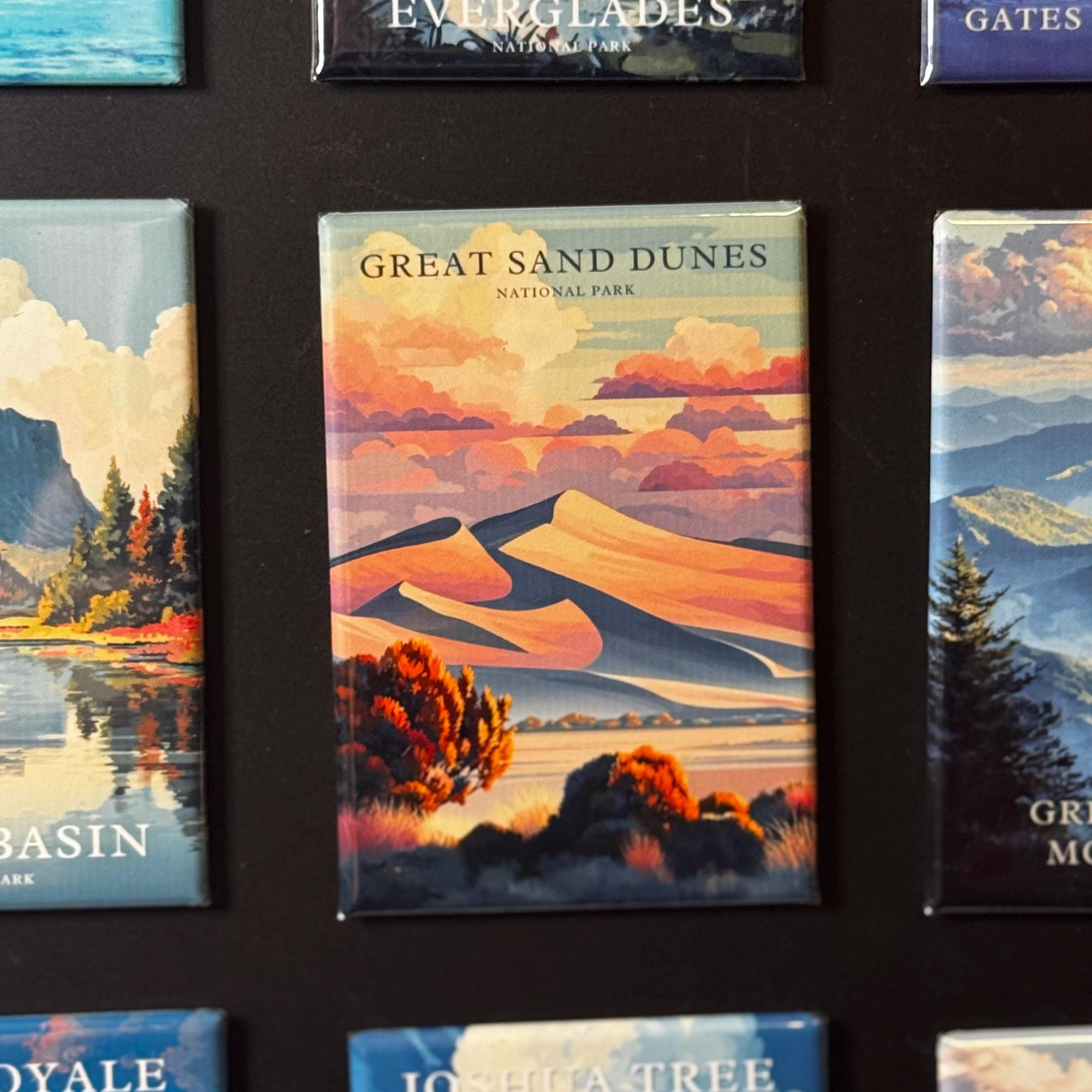 a collection of magnets with various scenic landscapes, including mountains, forests, and bodies of water. The magnets are arranged in a grid-like pattern, with each one depicting a different natural setting. The magnets are predominantly blue and green in color, creating a harmonious and visually appealing composition.