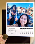 A person holding a photo of a family, with a calendar for the month of February visible.
