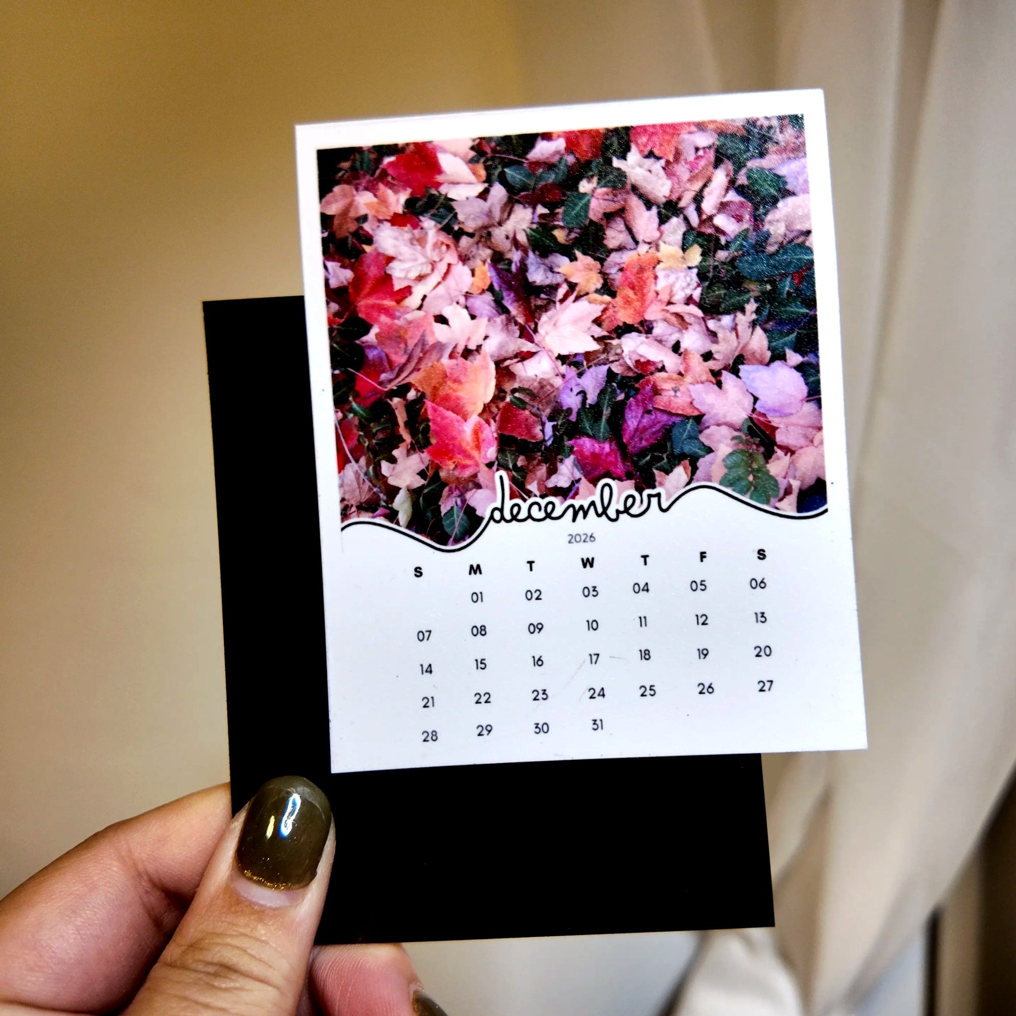 A person's hand holding a small calendar with a floral image on the cover.