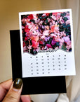 A person's hand holding a small calendar with a floral image on the cover.
