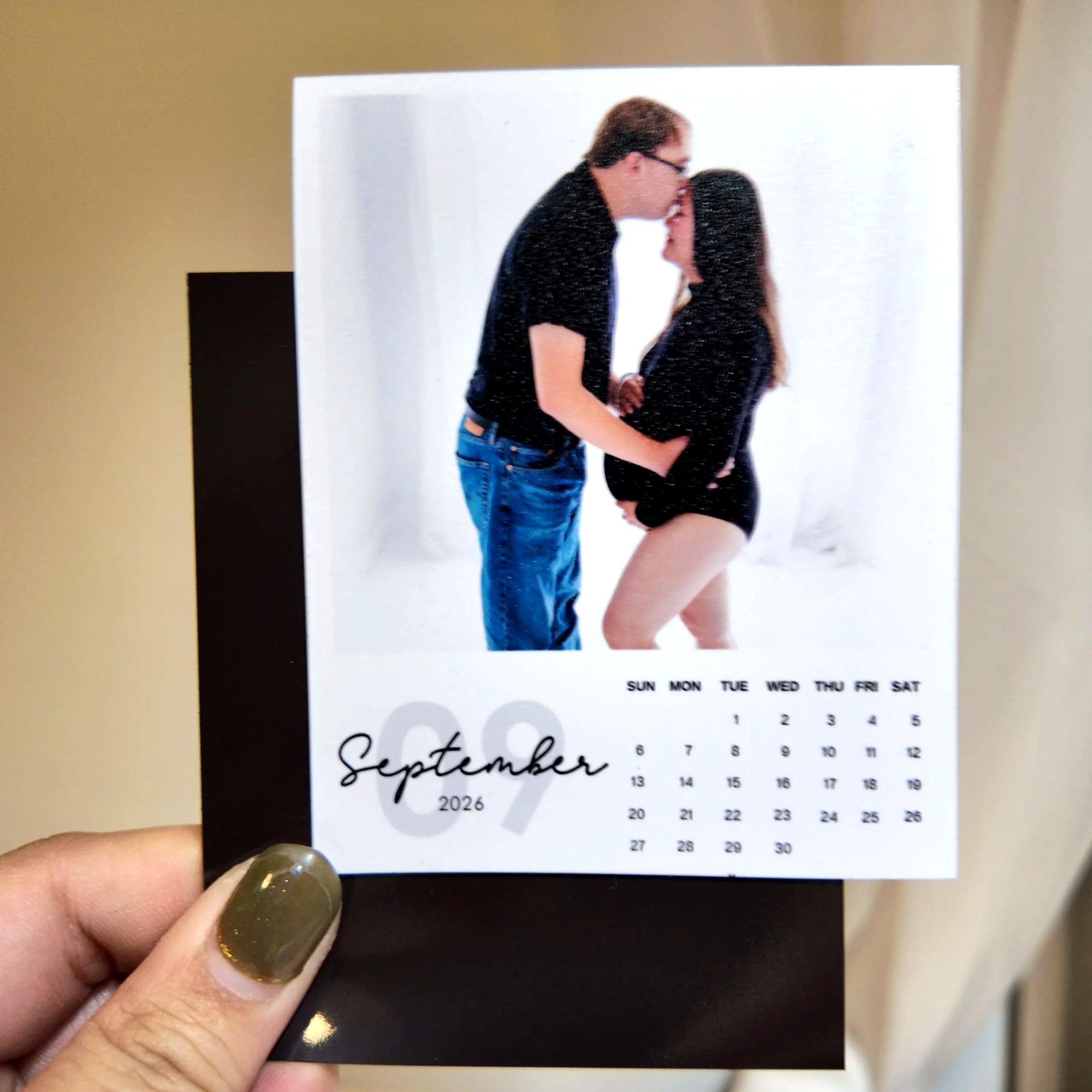 A hand holding a small photo frame with a photo of a couple embracing, and a calendar for September 2026.