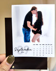 A hand holding a small photo frame with a photo of a couple embracing, and a calendar for September 2026.
