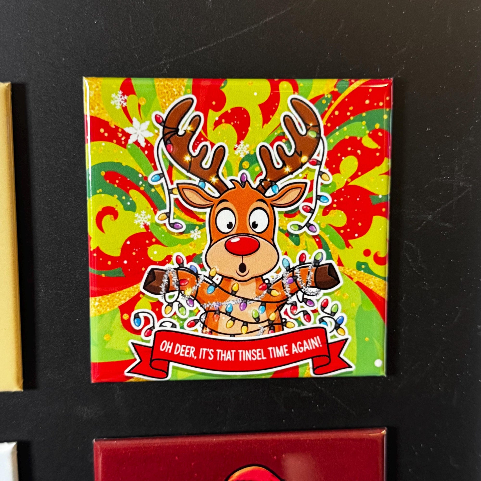 A colorful, festive Christmas-themed tile with a cartoon reindeer holding a banner that says "OH deer, it's that tinsel time again!"