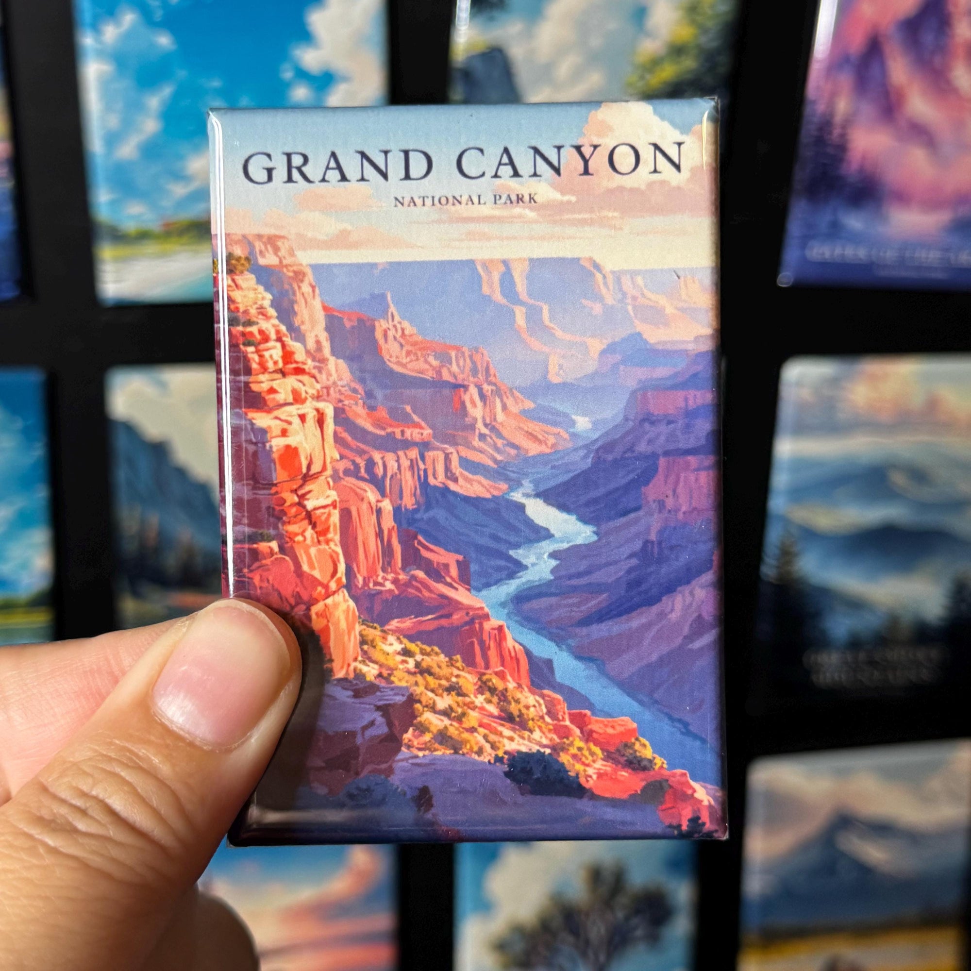 A hand holding a magnet with a colorful illustration of the Grand Canyon.