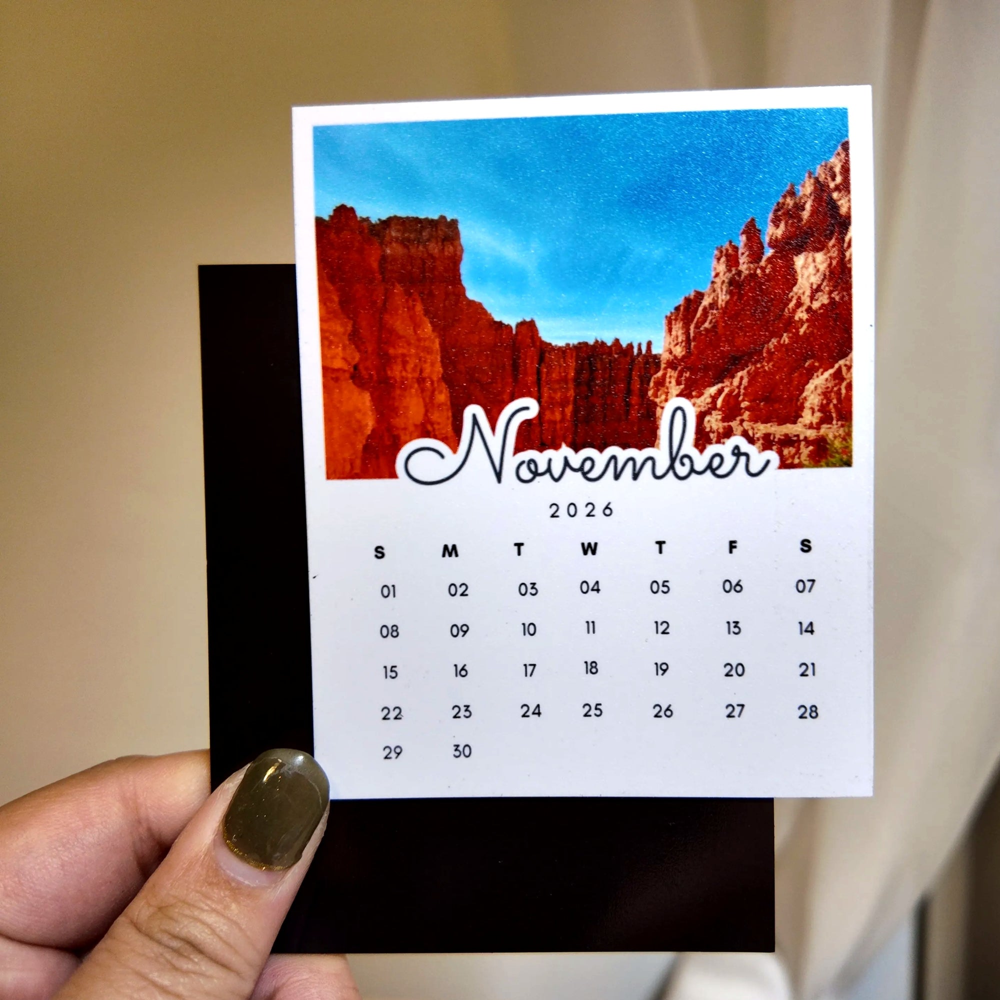 A person's hand holding a calendar card with a photo of a red rock formation and the word "November" written on it.