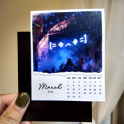 A person is holding a calendar for the month of March, which is for the year 2026. The calendar displays the days of the week and dates for each day.