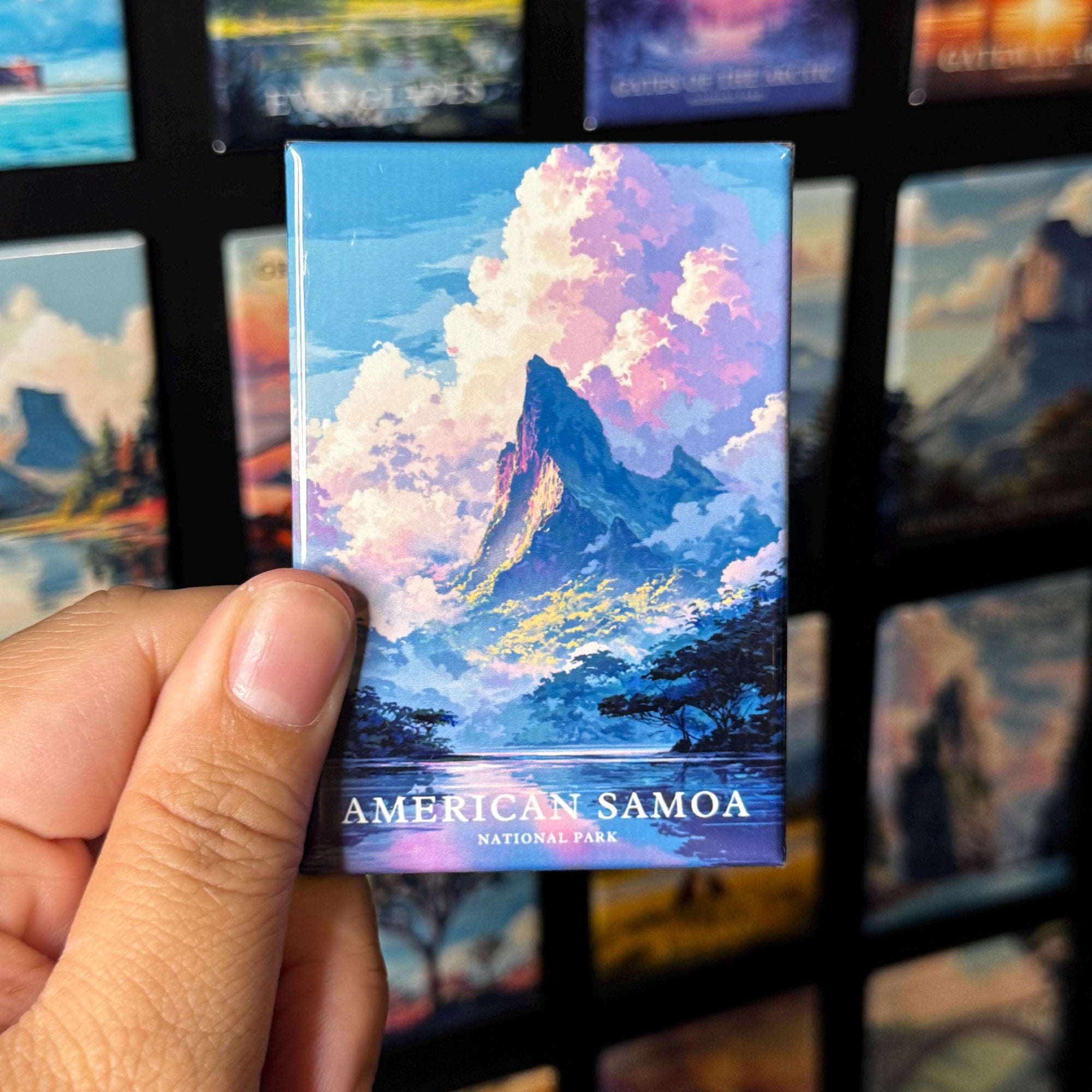 A hand holding a magnet with an illustration of a mountain landscape, specifically American Samoa, with the text "AMERICAN SAMOA NATIONAL PARK" printed on it.