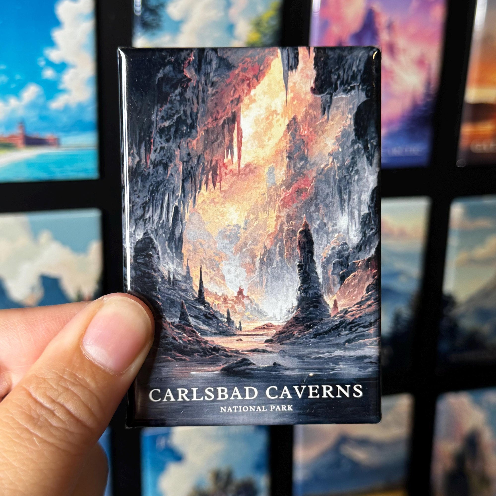 A hand holding a magnet with an illustration of a cave scene, with the text "CARLSBAD CAVENS NATIONAL PARK" printed on it.