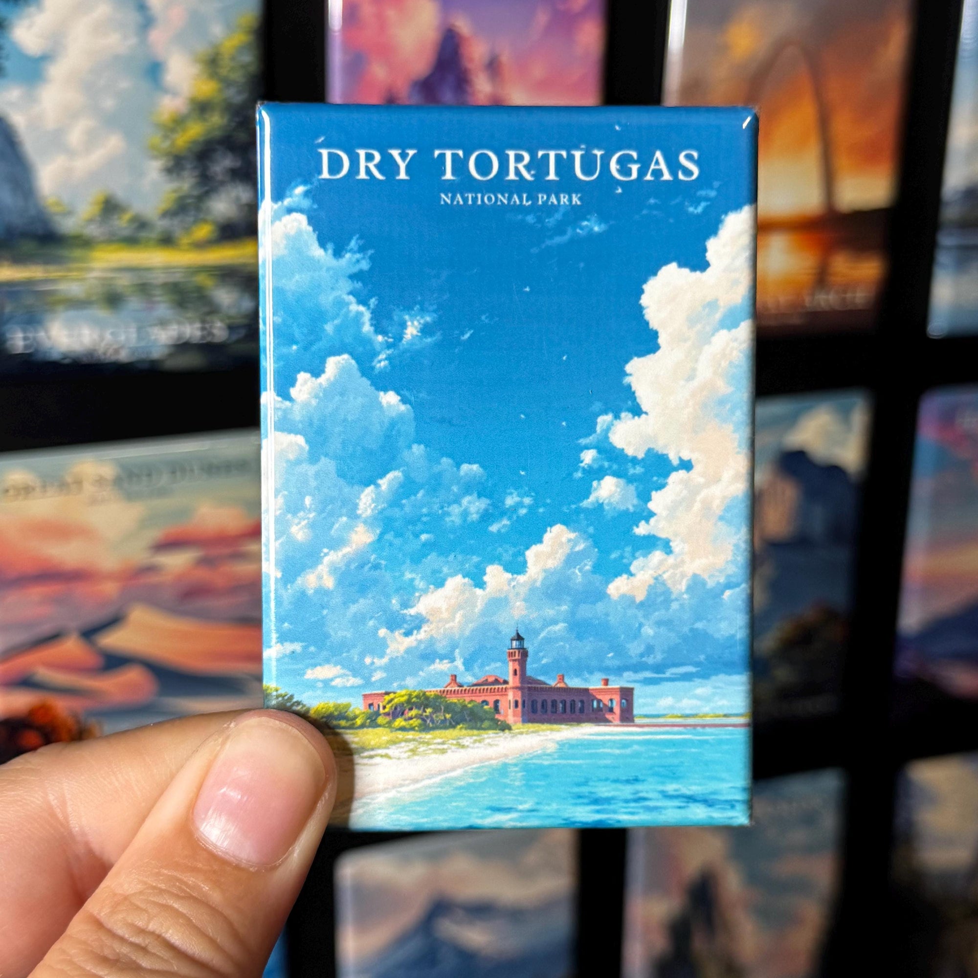 A hand holding a small magnet with a picture of a lighthouse and a beach, with the text "Dry Tortugas National Park" written on it.