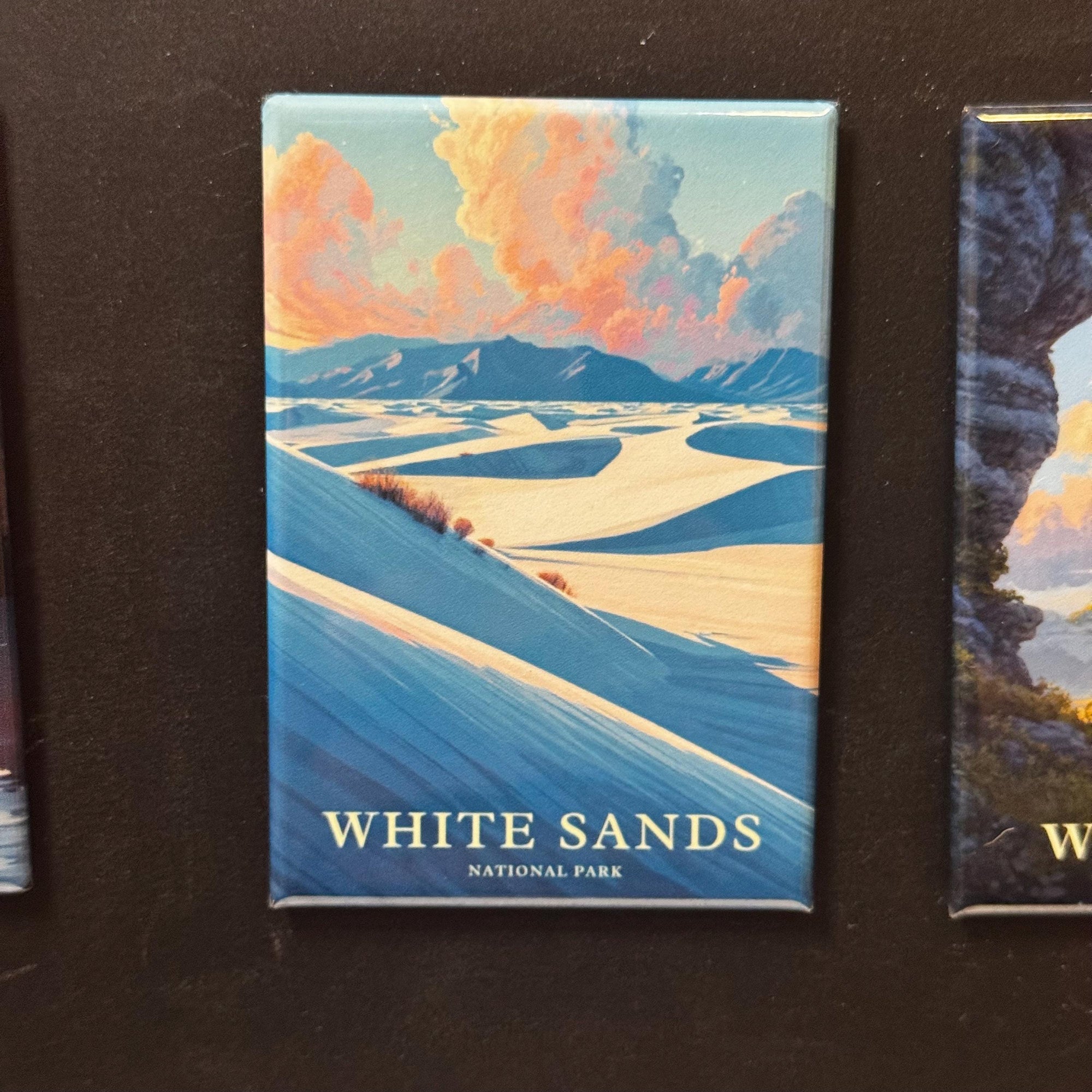 A framed magnet depicting a scenic landscape with mountains, clouds, and a body of water, with the text "WHITE SAND" and "NATIONAL PARK" printed on it.