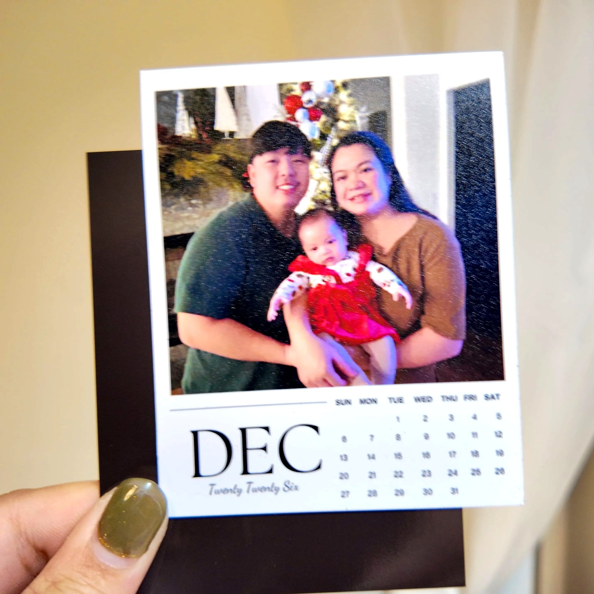 A hand holding a small calendar featuring a family photo of a man, woman, and child.