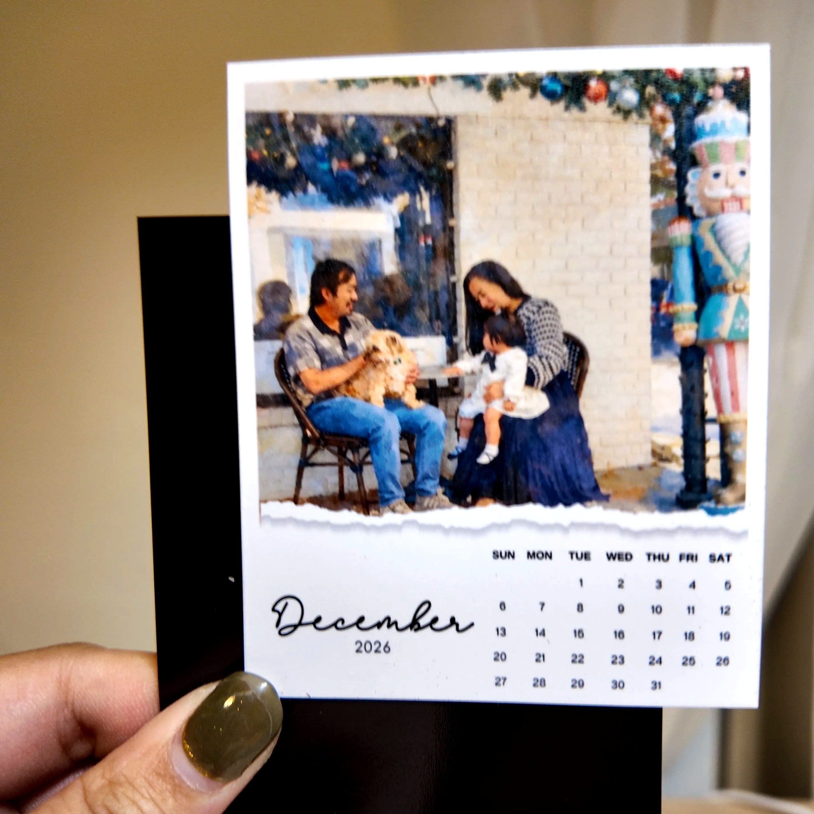 A person is holding a small photo frame containing a family portrait of a man, woman, and child sitting on a bench.