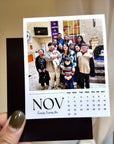 A person is holding a small calendar with a photo of a group of people on it.