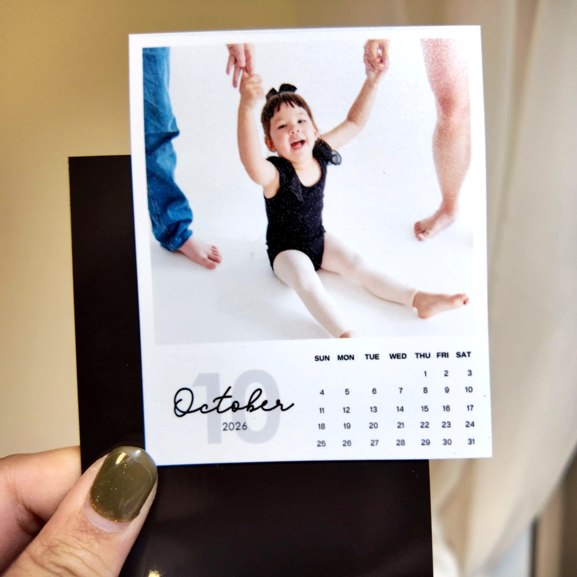 A person is holding a small calendar with a photo of a young girl in a black outfit, smiling and raising her arms.